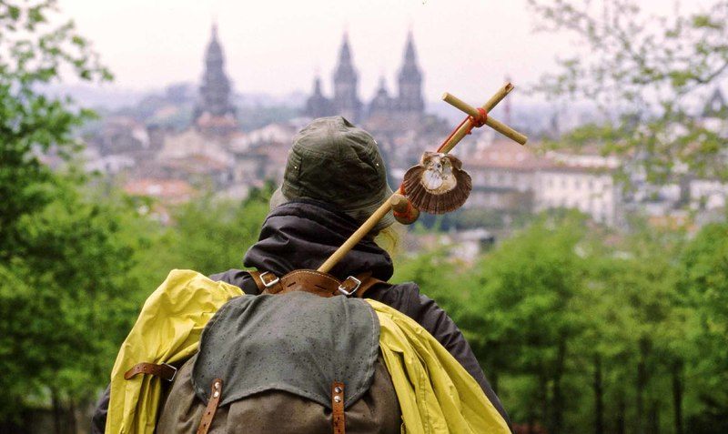 Peregrino con mochila y vieira de espaldas mirando la catedral de Santiago de Compostela.
